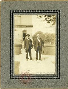 [Two men posing in front of a house]