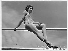 [Young woman wearing bathing suit sitting on Coney Island fence]