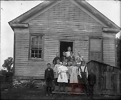 [Woman and children in front of wood fram building]
