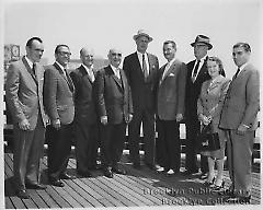 [Eight men and one woman standing on boardwalk]