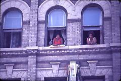[Two women looking out of building windows]