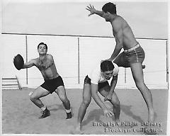 [Three young men playing football on beach]